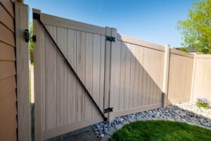 Tan vinyl gate and fence panels with black hinges and a diagonal support brace.