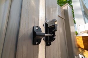 A black metal gate latch with a keyhole mounted on a light-colored vinyl fence.