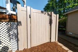 A tan vinyl privacy gate installed next to a wood deck with white lattice skirting.