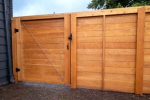 A double wooden gate made of horizontal planks, featuring a metal diagonal brace and a black latch mechanism.