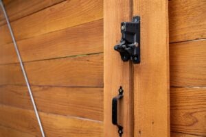 A black metal gate latch and handle mounted on a wooden gate.