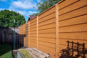 A tall, wood-plank fence runs along the side of a garden bed with a metal trellis.