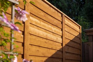 A wooden fence made of horizontal planks, with a trellis of pink flowers in the foreground.