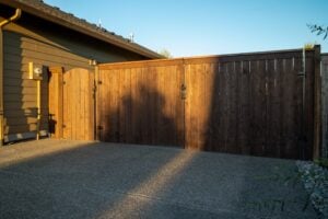 A wood fence with a double gate and a smaller arched gate next to the side of a house.