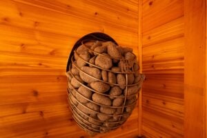 A wall-mounted sauna heater filled with stones in a metal basket against wooden walls.