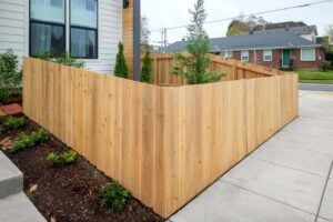 A newly installed cedar wood privacy fence wraps around the corner of a residential yard next to a sidewalk.