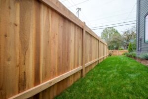 A tall, wooden privacy fence runs alongside a residential lawn.