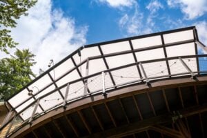 Low-angle view of a curved deck with a translucent roof and metal cable railing against a blue sky.