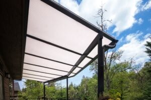 A white polycarbonate patio cover with a black metal frame attached to the side of a house.