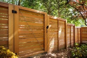 Horizontal slat wood fence and gate with metal hardware, framed by trees.