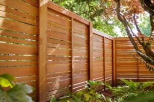 Horizontal wood slat fence panels set in a garden with trees and ferns.