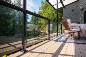 A deck with a glass railing, featuring a dining set on a blue patterned rug overlooking a yard.