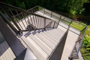 High-angle view of a gray composite deck with black railings and a hot tub tucked into the corner of the upper landing.