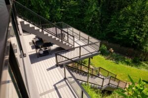 A multi-level composite deck with black metal railings and stairs overlooking a backyard and wooded area.