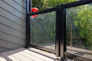 A deck with a black metal and glass railing, overlooking a wooden staircase and leafy trees with a red bird feeder hanging in the background.