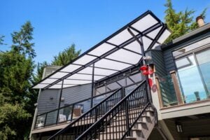A modern black metal-framed patio cover with a translucent roof installed over an elevated wooden deck and staircase.