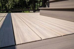 Light brown wood-grain decking with a set of stairs on the right and a black railing in the background.
