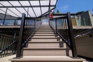 Outdoor deck stairs with black metal railings leading up to a house entrance covered by a translucent patio roof.