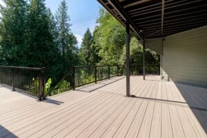 A spacious outdoor deck with composite wood-look planks and a black metal railing overlooking a forest.