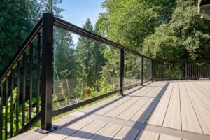 A composite deck with a black metal and glass panel railing overlooking a forest.