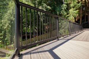 Black metal railing installed along the edge of a composite wood deck overlooking a wooded area.