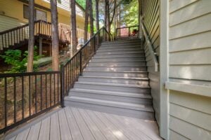 A set of outdoor stairs with gray composite decking leading upward between a house and a wooden deck.