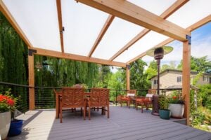 A wooden deck featuring a dining table with chairs, two lounge chairs with cushions, and a patio heater under a translucent pergola roof.