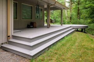A spacious grey deck with tiered stairs leading to a covered porch that features a hanging swing.