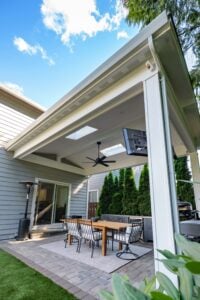 A covered patio with a wooden dining table, six chairs, a ceiling fan, and a mounted television.