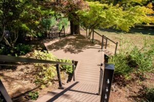 A composite deck with black metal railings features a wide landing and a staircase descending into a garden with trees and ferns.