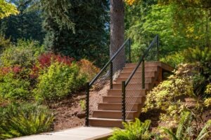 Outdoor stairs with dark metal railings and cable balusters set into a lush, wooded garden.