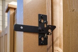 A black metal gate latch attached to a tan fence post.