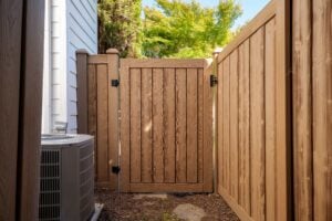 A tan composite gate set between two matching fence panels next to an air conditioning unit.