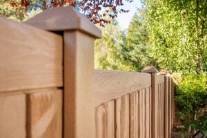 A brown wood-grain fence with square post caps in a garden setting.