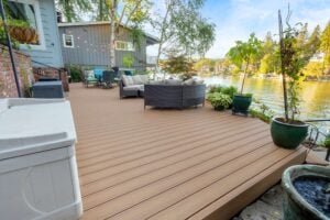 A spacious wood-plank deck overlooking a lake, furnished with outdoor seating, potted plants, and string lights.