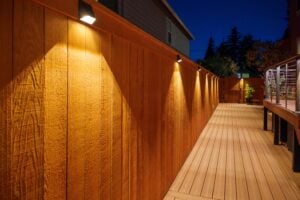 A wooden deck at night featuring a fence illuminated by a series of small, downward-facing wall lights.