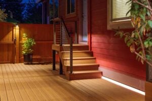 A wooden deck with a set of stairs leading to a doorway, illuminated by recessed strip lighting.