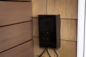 Black in-lite outdoor lighting transformer mounted on a cedar shingle wall.