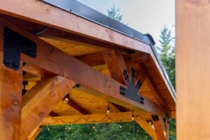 Timber-frame gazebo structure with decorative black metal brackets and hanging string lights.