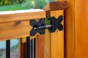 Adjustable black metal gate hinge mounted on a wooden railing.