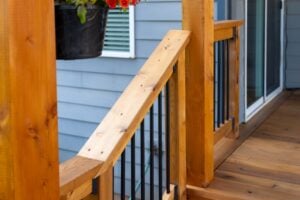 Wooden deck railing with a natural wood handrail and black metal balusters.
