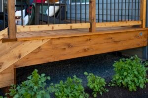 A newly constructed wooden deck with a black metal railing overlooking a gravel area with small green plants.