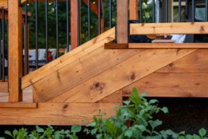Angled wood siding and stairs on a backyard deck with black metal railings.