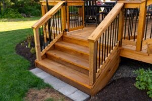 Wooden deck stairs with black metal railings leading up to a gated deck entrance.