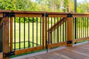 A wooden deck gate with black metal vertical balusters and hinges, overlooking a grassy backyard.