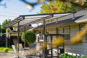 A metal patio cover extends from a house over a deck featuring a dining set and a large outdoor pet enclosure.