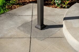 A dark metal support post centered on a square concrete patio patch.