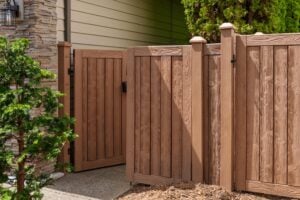 A brown wood-grain fence with a partially open gate next to a stone-accented house.