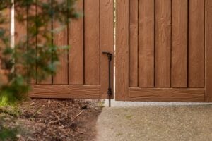 A closed brown wooden fence gate with a vertical metal drop-bolt latch.