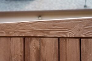 Close-up of a brown wood-grain textured fence with vertical panels and a horizontal top rail.